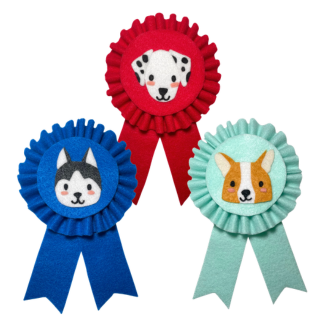 five award ribbons made out of felt material with dogs faces on them. blue ribbon with a husky. green ribbon with a spaniel. gold ribbon with a french bulldog. red ribbon with a dalmatian. mint green ribbon with a corgi.
